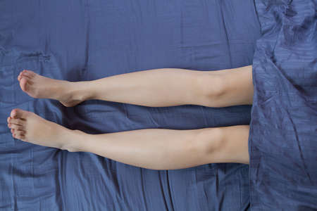 Close up Woman legs in bed under blanket. Beautiful shaved legs after spa and bath skin care...