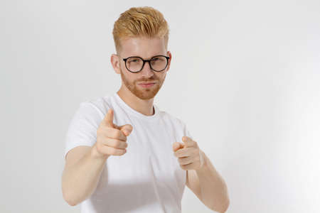Guy pointing on you by fingers isolated on white background. Young stylish redheaded man, red beard and glasses. White t shirt shows on you. Success and confidence concept. copyspace. selective focusの写真素材