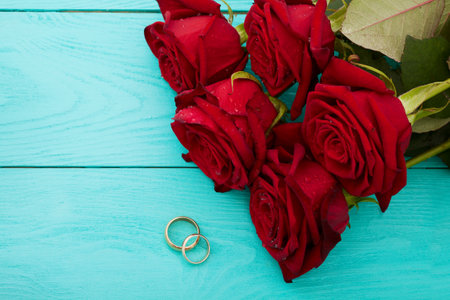 Wedding rings and red roses. Wedding bouquet on blue wooden background. selective focus. copy spaceの写真素材