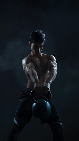 Handsome young man doing exercises with kettlebell on dark backgroundの素材