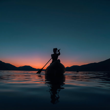 Silhouette of a woman paddling a canoe on a lake at sunsetの素材