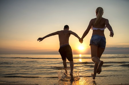 Couple running into water at sunriseの写真素材
