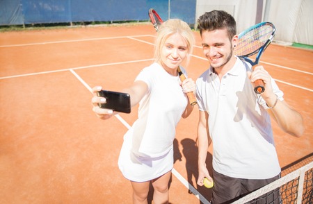 Couple taking a selfie on a tennis courtの写真素材