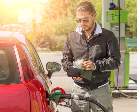 Young man filling car at gasoline tank while counting moneyの写真素材