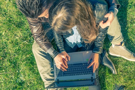 Couple sitting on grass after a romantic tour with bicycle - Lovers looking at computer while...