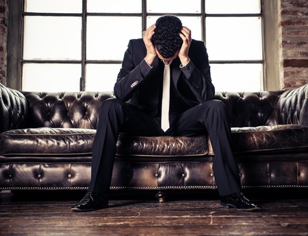 Depressed business man sitting on sofa - Negative image of young sad personの写真素材