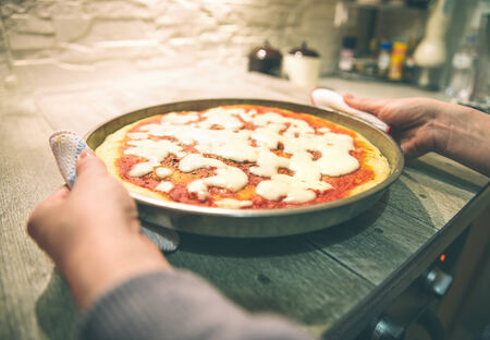 Woman taking out handmade pizza margherita from oven - Candid image of italian pizza preparationの写真素材