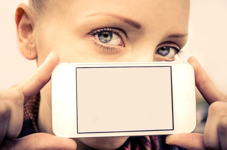 Portrait of young beautiful girl with blue eyes holding a smart phone - Blank phone screen and pretty modelの写真素材