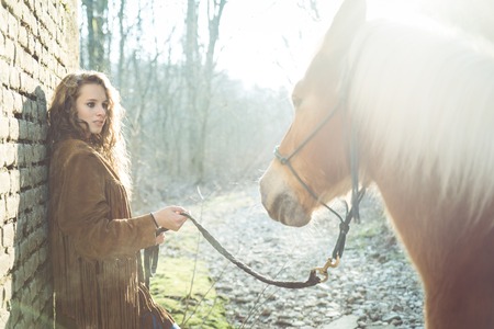 Beautiful woman holding a brown horse - Pretty caucasian model with stallion outdoorsの写真素材
