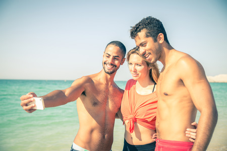 Group of friends on the beach smiling at camera - Four people of different ethnic having fun and...