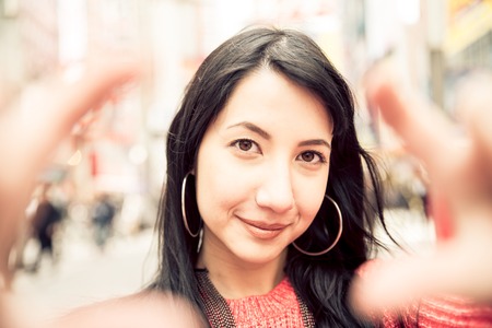 Beautiful woman making a frame with fingers in front of face - Brunette girl taking a picture in Akihabara,Tokyoの写真素材