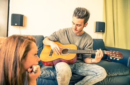 Young man playing guitar for his girlfriend at home - family,recreation,leisure,togetherness conceptの写真素材