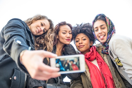 Group of attractive young women of different ethnics taking a selfie - Students having fun - Best friends spending time together - Tourists photographing on a city tourの写真素材