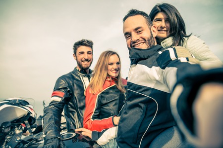 Bikers taking selfie with camera - Four smiling friends driving racing motorcycles with their girlfriends  - Two happy couples stop in a panoramic view point and photographing themselvesの写真素材