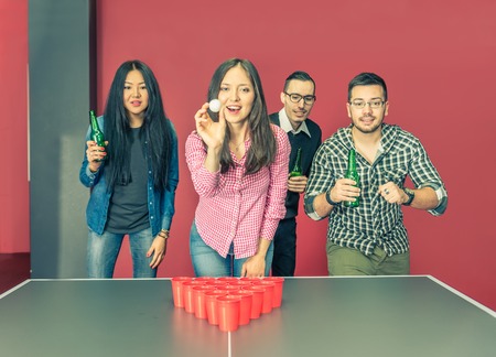 Four young college students playing at beer pong in a hostel - Group of multiracial friends drinking beer and having fun -concepts about youth,party and social gatheringの写真素材