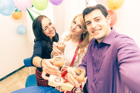 Group of friends celebrating birthday - Young man holding camera and taking a picture with camera while at his girlfriend's party - Young attractive people at party toasting champagne glasses and having funの写真素材