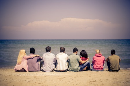Group of mutiracial friends sitting on the beach and looking at horizon - Young students on a summer vacationの写真素材