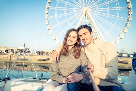 Beautiful couple of lovers sailing on a boat - Young attractive man holding a selfie stick and taking a picture - Two fashion models posing on a sailing boat at sunsetの写真素材
