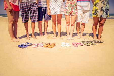Group of friends on the beach with colored slippers on the sand - Tourists on vacation on a tropical...