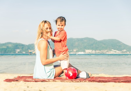 Mom playing with her handsome son on the beach - Happy family on vacation on a tropical beachの写真素材