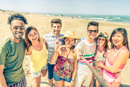 Multiethnic group of friends enjoying vacation  and taking a picture with selfie stick - Mixed group of several people having fun on the beachの写真素材