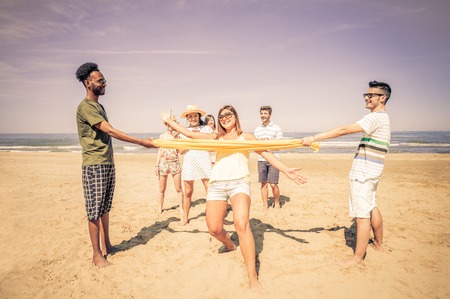 Group of happy and playful friends playing at limbo on the beach - Tourists on vacation on a tropical travel destination on summertimeの写真素材