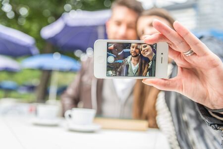 Couple sitting at restaurant table taking a self portrait with phone - Friends in a bar looking at cell phoneの写真素材