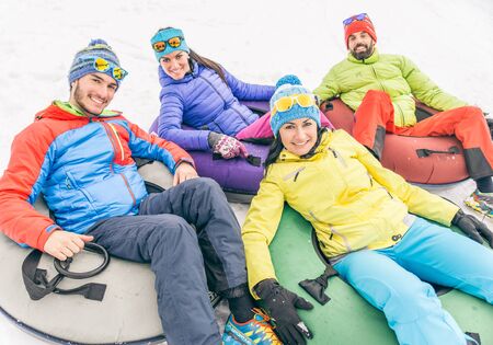 Friends driving sleds on snow - Four happy tourists sledding downhill during winter vacation