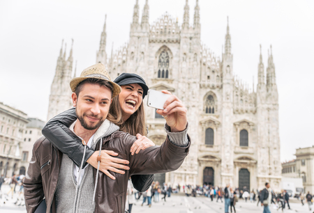 Happy tourists taking a self portrait with phone in front of Duomo cathedral,Milan - Couple travelling in Italyの写真素材