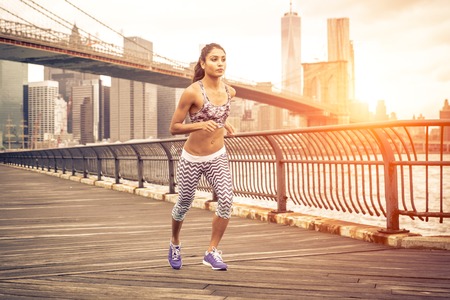 beautiful asian woman running in New york at sunset time. Brooklyn bridge and Manhattan skyline in...
