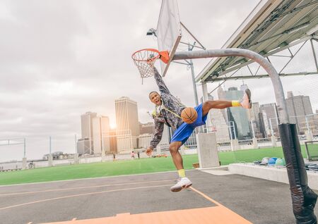Sportive man hanging from the basket and looking down triumphant at camera after a slam dunk - Basketball player scoring for his teamの写真素材