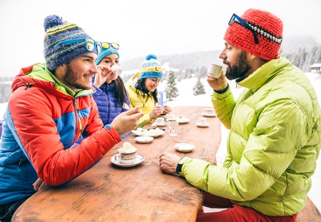 Group of mult-ethnic friends drinking hot chocolate and coffee - Happy people partying and eating in home garden - Young active adults in a restaurant on winter vacationの写真素材