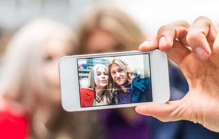 Couple taking selfie with cellular phone - Two friends photographing themselves for a social...