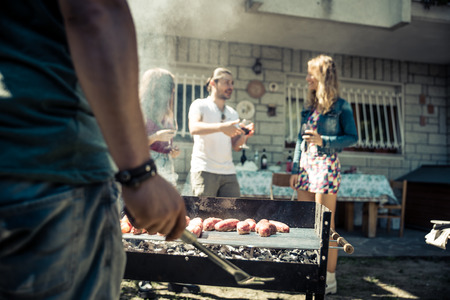 Friends in home garden grilling meat and having fun - Group of people at barbecue party drinking wineの写真素材