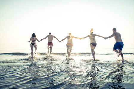 Group of friends running on the beach at sunset - Summer vacation on a tropical beachの写真素材