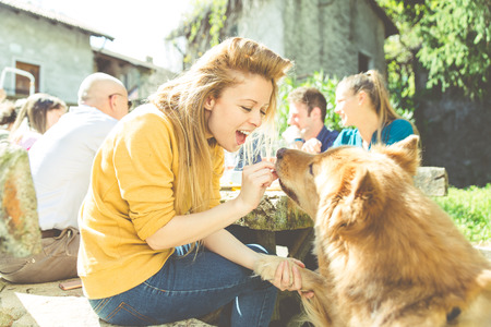 Group of friends eating outdoor. Woman feeding her dogの写真素材