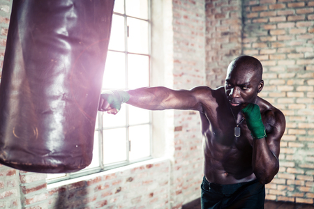 Black boxer punching the heavy bag in the gymの写真素材