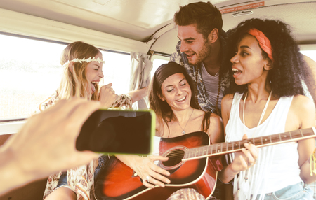 Hippie friends having fun into a vintage van, playing the guitar and singing songsの写真素材