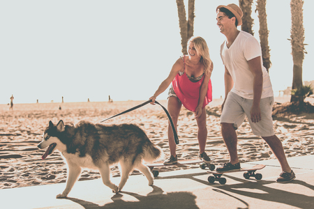 Couple having fun with their skates and playful huskyの写真素材