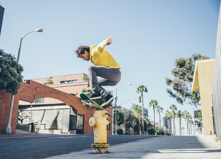 Cool skateboarder jumping over a hydrant on the streets - Afroamerican guy jumping with his skate and performing a trickの写真素材