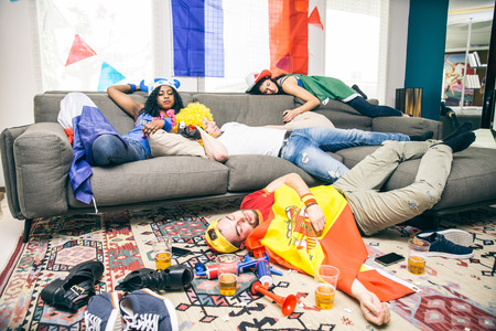 Group of friends sleeping in a living room after party - Drunk supporters resting after celebrating their teams at a sport eventの写真素材
