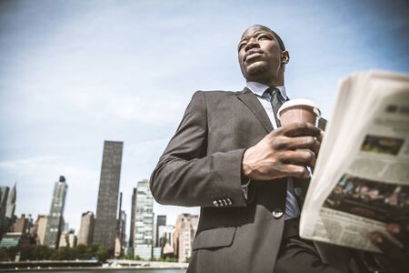 Confident businessman. Successful young man in full suit reading financial news on newspaper and drinking a cup of coffeeの写真素材