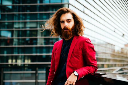 Fashion portrait of a young hipster man walking outdoors with a red formal suit - Unusual businessman going to workの写真素材