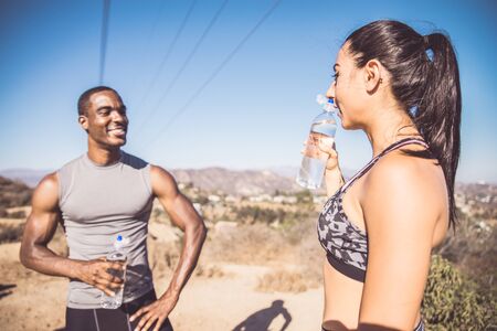 Couple of runners resting while training and drinking water - Multi-ethnic couple doing sport outdoorsの写真素材