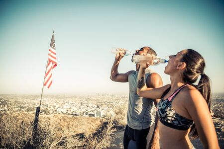 Couple of runners resting while training and drinking water - Multi-ethnic couple doing sport...