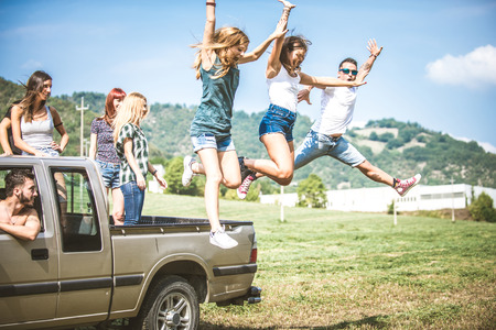 Group of friends driving on the back of pick-up car and having fun - People on vacation and enjoying an excursion in the natureの写真素材