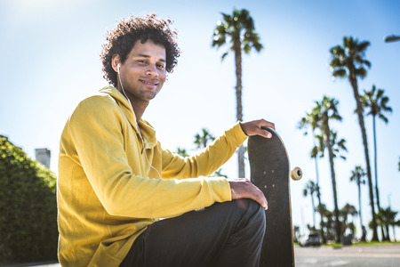 Cool skateboarder outdoors - Afroamerican guy jumping with his skate and performing a trickの写真素材