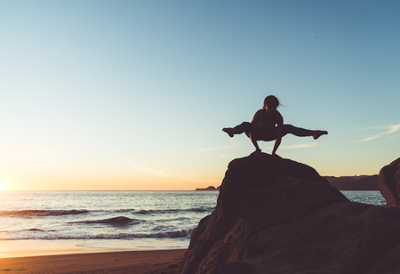 Woman training yoga on the beach at sunsetの写真素材