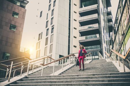 Fashion portrait of a young hipster man walking outdoors with a red formal suit - Unusual businessman going to workの写真素材