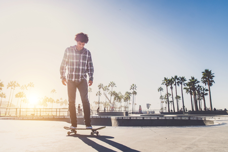 Cool skateboarder outdoors - Afroamerican guy jumping with his skate and performing a trickの写真素材